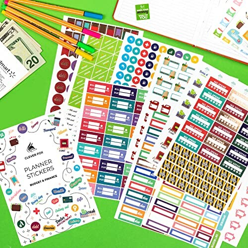 Colorful planner stickers for budgeting and finance on a green surface with pens and money.